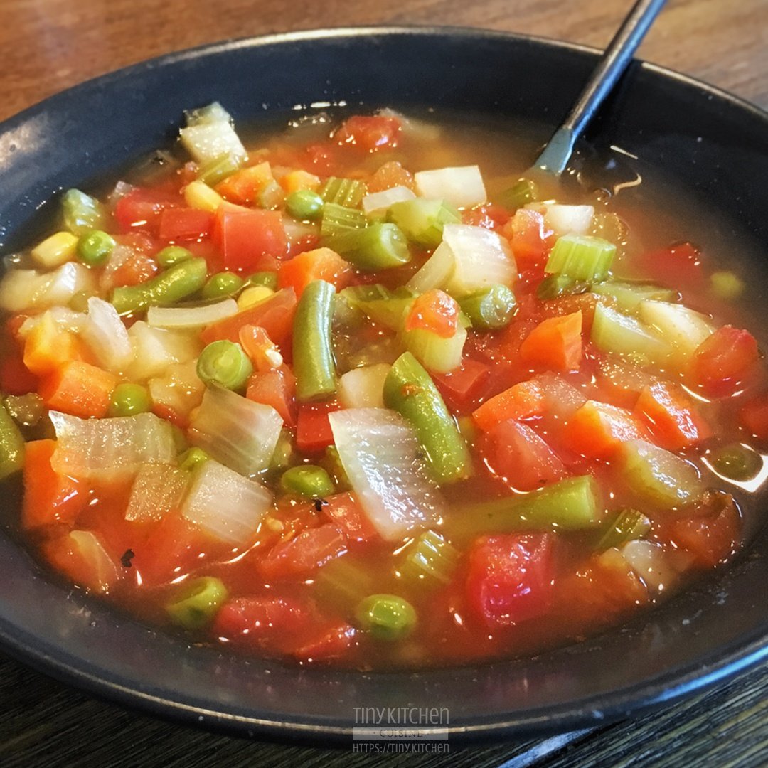 A bowl of homemade vegetable soup filled with delicious veggies like potato, peas, tomato, onion, and green beans.
