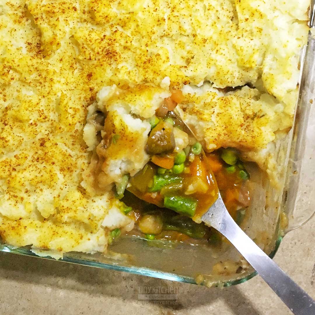 Vegetarian Shepherd's Pie in a casserole dish with a spoon filled with mushrooms, carrots, onions, celery, peas, and gravy.