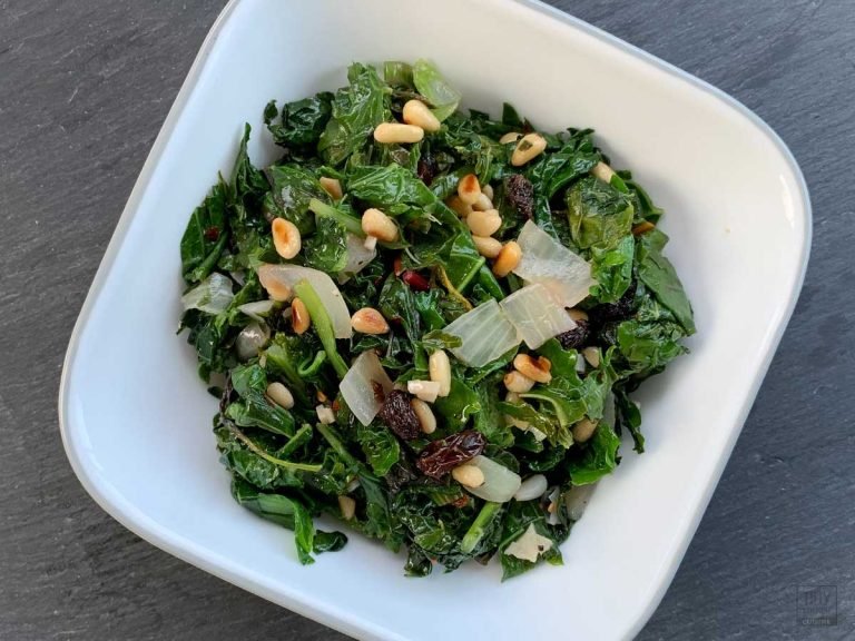 Bowl of mixed braised greens topped with toasted pine nuts and raisins.
