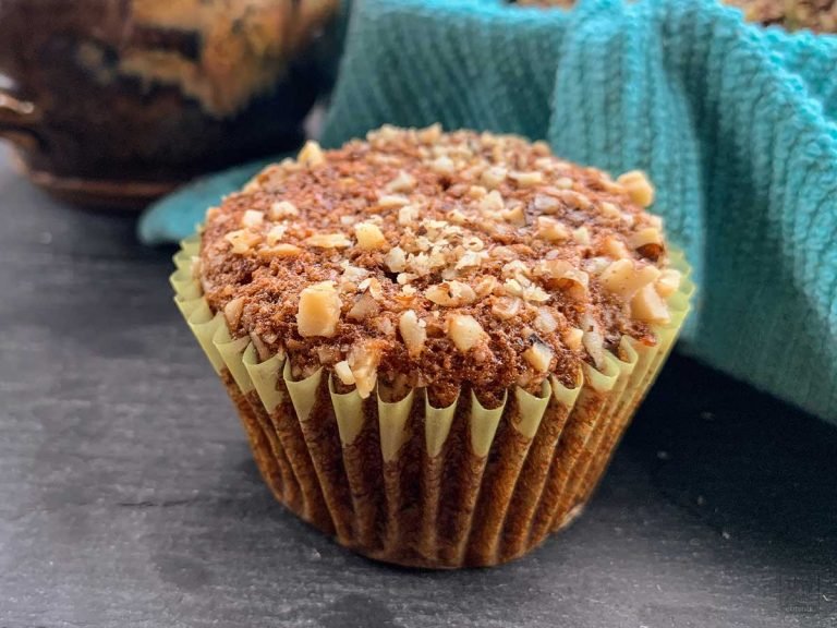 Close up of a banana nut muffin topped with walnuts and a blue cloth lined basket of muffins in the background.